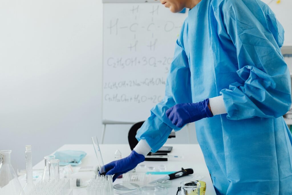 Scientist in protective clothing working in lab with chemical formulas on whiteboard.