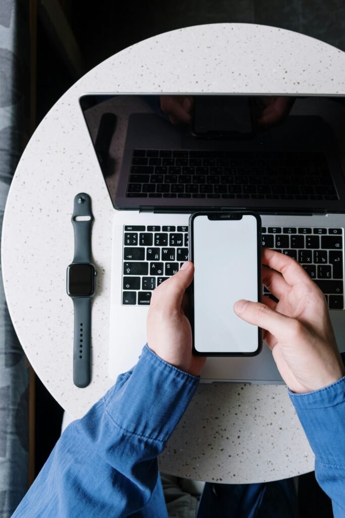 Top view of a person using a smartphone above a laptop with a smartwatch on the table.